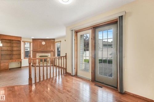 Hardwood flooring throughout featuring a wood railing and a built-in bookshelf - 8008 158 Avenue Nw, Edmonton, AB - Indoor Photo Showing Other Room With Fireplace