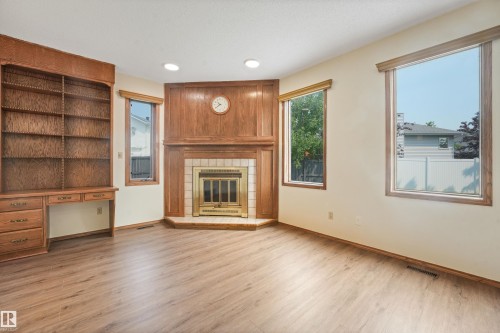 Corner fireplace with a tile surround and wood paneling, wood-finish flooring, built-in shelving, and multiple windows - 8008 158 Avenue Nw, Edmonton, AB - Indoor Photo Showing Living Room With Fireplace