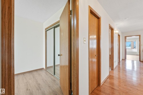 Hardwood-finish flooring extending through a hallway with multiple wood-paneled doors and a room featuring wood-finish flooring and a mirrored closet - 8008 158 Avenue Nw, Edmonton, AB - Indoor Photo Showing Other Room