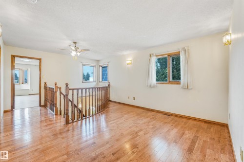 Hardwood flooring throughout featuring a wood baluster railing, multiple windows providing natural illumination, and a ceiling fan with integrated lighting - 8008 158 Avenue Nw, Edmonton, AB - Indoor Photo Showing Other Room