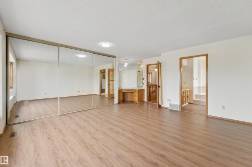 Expansive room featuring wood-finish flooring, a full wall of mirrored closet doors, a built-in wooden vanity with mirror, and recessed lighting - 8008 158 Avenue Nw, Edmonton, AB - Indoor Photo Showing Other Room