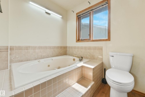 Soaking tub with a tiled surround, integrated steps, and brass fixtures - 8008 158 Avenue Nw, Edmonton, AB - Indoor Photo Showing Bathroom