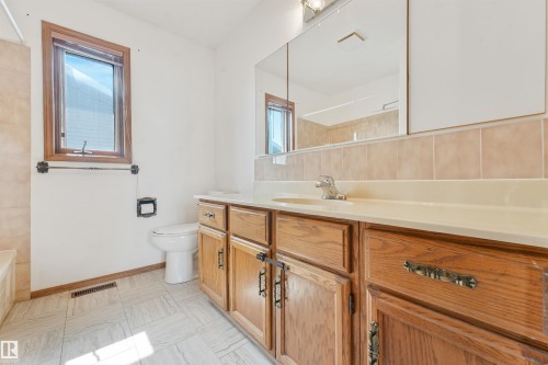 Bathroom featuring a single vanity with wood cabinetry, a light-toned countertop, and a large wall-mounted mirror - 8008 158 Avenue Nw, Edmonton, AB - Indoor Photo Showing Bathroom
