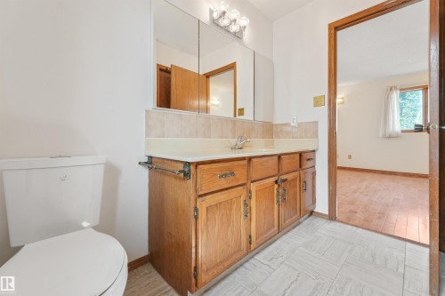 Bathroom featuring a wood-finish vanity with a built-in sink, a large mirrored medicine cabinet, and a three-light vanity fixture - 8008 158 Avenue Nw, Edmonton, AB - Indoor Photo Showing Bathroom