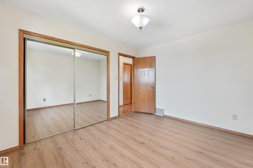 Room featuring wood-finish flooring, mirrored closet doors with wood trim, and a semi-flush ceiling light fixture - 8008 158 Avenue Nw, Edmonton, AB - Indoor Photo Showing Other Room