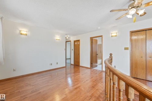 Hardwood-finish flooring extending throughout, complemented by a wooden banister - 8008 158 Avenue Nw, Edmonton, AB - Indoor Photo Showing Other Room
