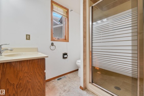 Bathroom featuring a wood-finish vanity with an integrated sink, a window with wood trim, and a shower enclosure with frosted glass - 8008 158 Avenue Nw, Edmonton, AB - Indoor Photo Showing Bathroom