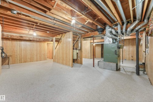 Spacious unfinished basement featuring exposed ceiling joists and ductwork, light-toned carpeting, wood-paneled walls, and a visible furnace system - 8008 158 Avenue Nw, Edmonton, AB - Indoor Photo Showing Basement