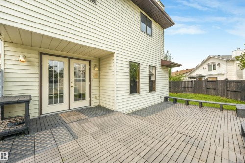 Spacious rear patio featuring a grid-patterned surface, built-in benches, and double glass-paneled doors - 8008 158 Avenue Nw, Edmonton, AB - Outdoor With Deck Patio Veranda With Exterior