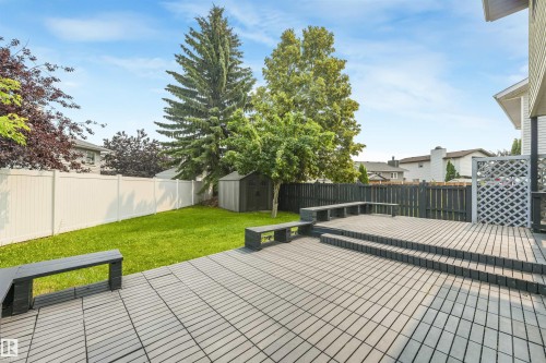 Multi-level composite deck featuring integrated bench seating, privacy lattice, and steps descending to a green lawn - 8008 158 Avenue Nw, Edmonton, AB - Outdoor With Backyard