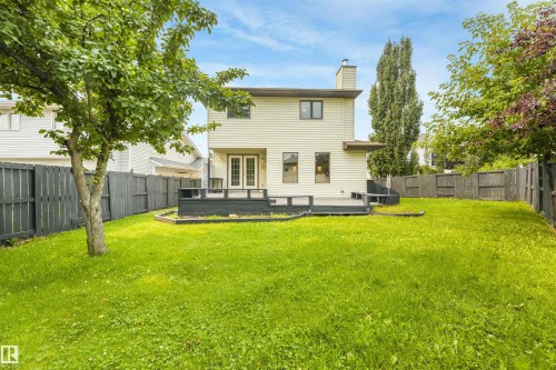 Expansive fenced backyard featuring a substantial wood deck, established shade trees, and a two-story exterior with siding - 8008 158 Avenue Nw, Edmonton, AB - Outdoor With Backyard