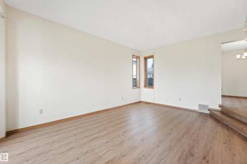 Spacious living area featuring wood-finish flooring, light-toned walls, and natural wood-framed windows - 8008 158 Avenue Nw, Edmonton, AB - Indoor Photo Showing Other Room