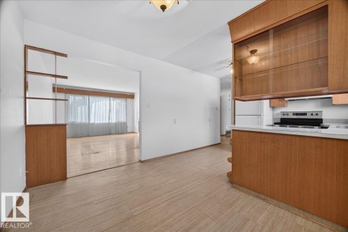 Wood-finish flooring throughout, with a built-in shelving unit, overhead lighting, and an open concept kitchen featuring wood cabinetry, white countertops, and a range cooker - 6104 92 Avenue Nw, Edmonton, AB 
