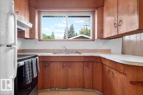 Wood-finish cabinetry, white countertops, built-in sink, white appliances, and a window providing natural light - 6104 92 Avenue Nw, Edmonton, AB 