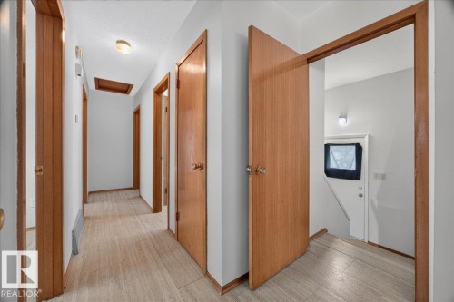 Wood-finish flooring throughout the hallway, light gray wall paint, natural wood-finish interior doors, and a ceiling-mounted light fixture - 6104 92 Avenue Nw, Edmonton, AB 