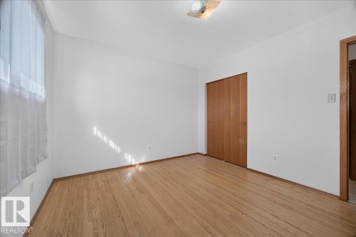 Hardwood flooring throughout, white painted walls, and built-in closet with wood-finish bi-fold doors - 6104 92 Avenue Nw, Edmonton, AB 