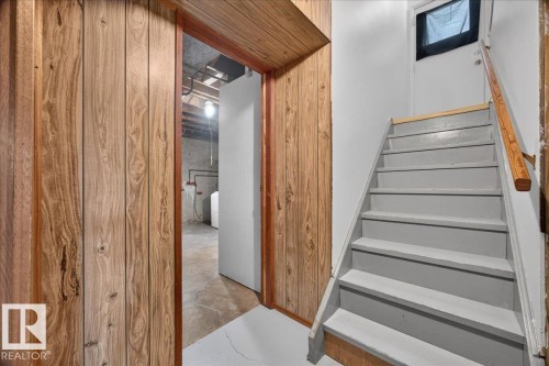 Wood paneling accent wall, painted staircase with wood handrail, and interior door with frosted window - 6104 92 Avenue Nw, Edmonton, AB 