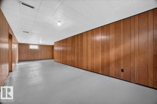 Expansive interior space featuring wood-panel walls, a drop ceiling, and a painted concrete floor - 6104 92 Avenue Nw, Edmonton, AB 