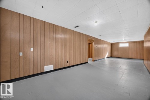 Expansive interior space featuring wood paneling, painted concrete flooring, and a drop ceiling - 6104 92 Avenue Nw, Edmonton, AB 