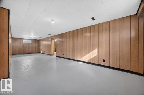 Expansive room featuring wood-finish wall paneling, a light-toned ceiling, and a single window - 6104 92 Avenue Nw, Edmonton, AB 