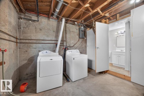 Concrete flooring, exposed ceiling joists, laundry hookups, white vanity with mirror and lighting, and a white sink - 6104 92 Avenue Nw, Edmonton, AB 