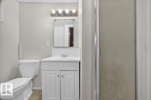 White vanity with a single basin sink, wall-mounted mirror, and overhead four-bulb light fixture - 6104 92 Avenue Nw, Edmonton, AB 