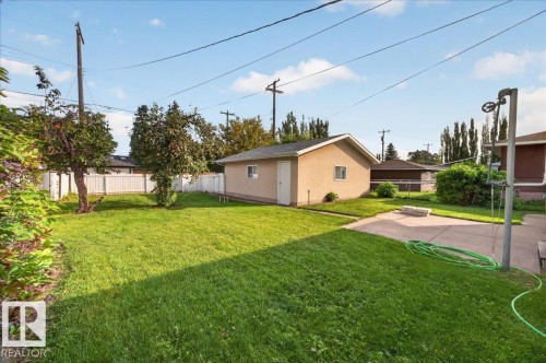 Expansive backyard featuring a manicured lawn, established trees, concrete patio, and detached garage - 6104 92 Avenue Nw, Edmonton, AB 