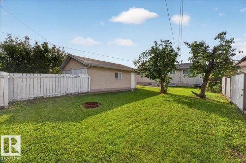 Expansive grassy yard with mature trees, a privacy fence, and an exterior building with a window - 6104 92 Avenue Nw, Edmonton, AB 