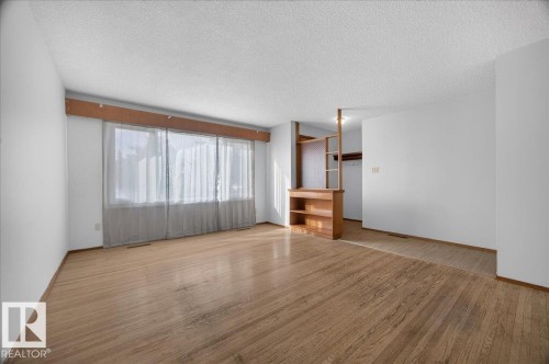 Hardwood flooring throughout, built-in wooden shelving, and a large window with sheers - 6104 92 Avenue Nw, Edmonton, AB 