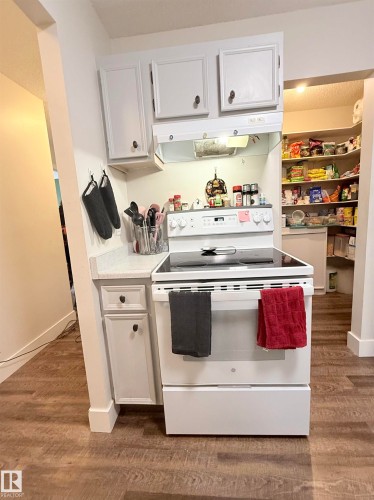 Wood-finish flooring, white cabinetry with dark hardware, solid surface countertops, white electric range, and a corner pantry with shelving - #89 2703 79 St Nw, Edmonton, AB 