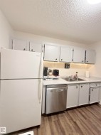 White upper and lower cabinetry, stainless steel dishwasher, double basin sink with a chrome faucet, wood-finish flooring, and light-toned countertops - 