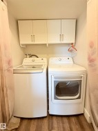 Laundry area featuring wood-finish flooring and white upper cabinetry - 