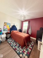 Wood-finish flooring with a contrasting accent wall, featuring a window with drapes and a modern ceiling light fixture - 