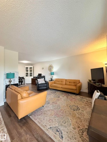 Spacious living area featuring wood-finish flooring, a fireplace with a light-toned surround, recessed lighting, and a built-in cabinet with glass-front doors - #89 2703 79 St Nw, Edmonton, AB 
