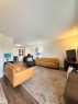 Spacious living area featuring wood-finish flooring, a fireplace with a light-toned surround, recessed lighting, and a built-in cabinet with glass-front doors - #89 2703 79 St Nw, Edmonton, AB 