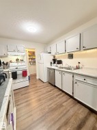 Wood-finish flooring throughout the kitchen, white cabinetry with dark hardware, stainless steel dishwasher, and a double basin sink - 