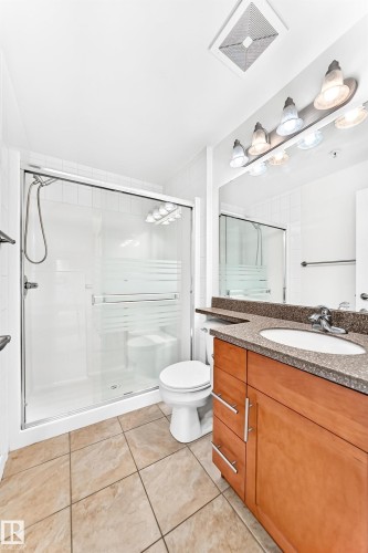 Bathroom featuring a glass-enclosed shower, light wood-finish vanity with an integrated sink, stone-finish countertop, and tiled flooring - #307 1003 Gault Bv Nw, Edmonton, AB - Indoor Photo Showing Bathroom