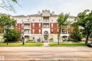 Residential building with a brick and stone facade, featuring multiple balconies with white railings, a central arched entryway, and dormer windows - #307 1003 Gault Bv Nw, Edmonton, AB  - Outdoor With Balcony With Facade 