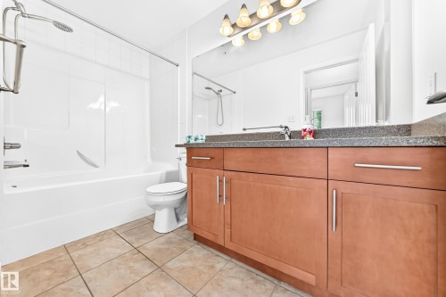 Contemporary bathroom featuring a light wood-finish vanity with a dark countertop and chrome hardware - #307 1003 Gault Bv Nw, Edmonton, AB - Indoor Photo Showing Bathroom