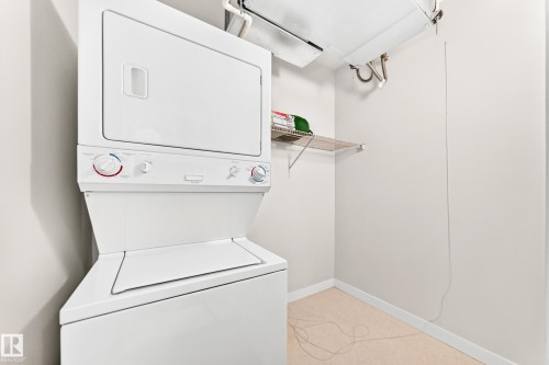 Dedicated laundry area featuring a stacked washer and dryer unit, neutral wall paint, white baseboards, and a wire shelving unit - #307 1003 Gault Bv Nw, Edmonton, AB - Indoor Photo Showing Laundry Room