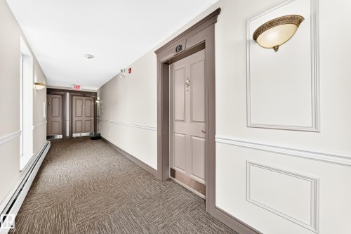 Hallway featuring wainscoting, decorative wall sconces, patterned carpet flooring, and paneled doors with substantial trim - #307 1003 Gault Bv Nw, Edmonton, AB - Indoor Photo Showing Other Room