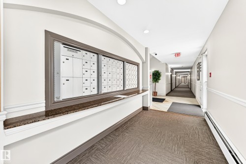 Mailbox station with a granite-look counter, decorative archway, wainscoting, and patterned carpet flooring - #307 1003 Gault Bv Nw, Edmonton, AB - Indoor Photo Showing Other Room
