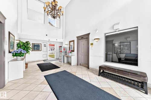 Spacious entry foyer featuring high ceilings with a multi-tiered chandelier, tiled flooring, and a large interior window - #307 1003 Gault Bv Nw, Edmonton, AB - Indoor