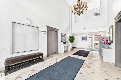 Grand foyer featuring a high ceiling, a large chandelier, and neutral tile flooring - #307 1003 Gault Bv Nw, Edmonton, AB - Indoor Photo Showing Other Room