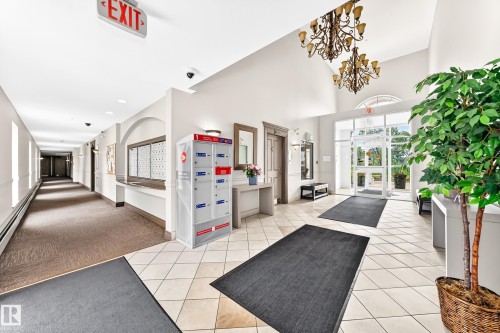 Spacious entry lobby featuring tiled flooring, a high vaulted ceiling, and dual chandelier lighting fixtures - #307 1003 Gault Bv Nw, Edmonton, AB - Indoor Photo Showing Other Room