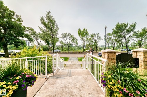 Concrete pathway with white metal railings, flanked by decorative planters with colorful flowering plants - #307 1003 Gault Bv Nw, Edmonton, AB - Outdoor