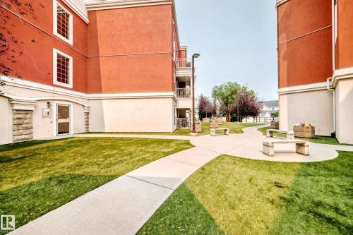 Landscaped courtyard featuring a concrete pathway, green lawn, and several stone benches - #307 1003 Gault Bv Nw, Edmonton, AB - Outdoor