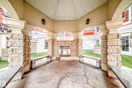 Stone and stucco-clad outdoor gazebo featuring an integrated grill station and built-in stone benches - #307 1003 Gault Bv Nw, Edmonton, AB -  Photo Showing Other Room With Fireplace