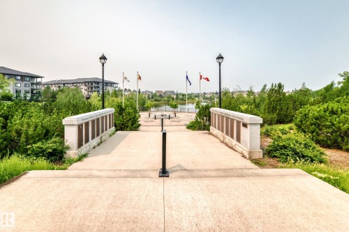 Paved pedestrian pathway bordered by decorative stone monuments, established landscaping, and traditional streetlights - #307 1003 Gault Bv Nw, Edmonton, AB - Outdoor