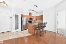 Open-concept kitchen featuring light-toned cabinetry, stainless steel appliances, and a breakfast bar with stone countertops - #307 1003 Gault Bv Nw, Edmonton, AB  - Indoor Photo Showing Other Room 